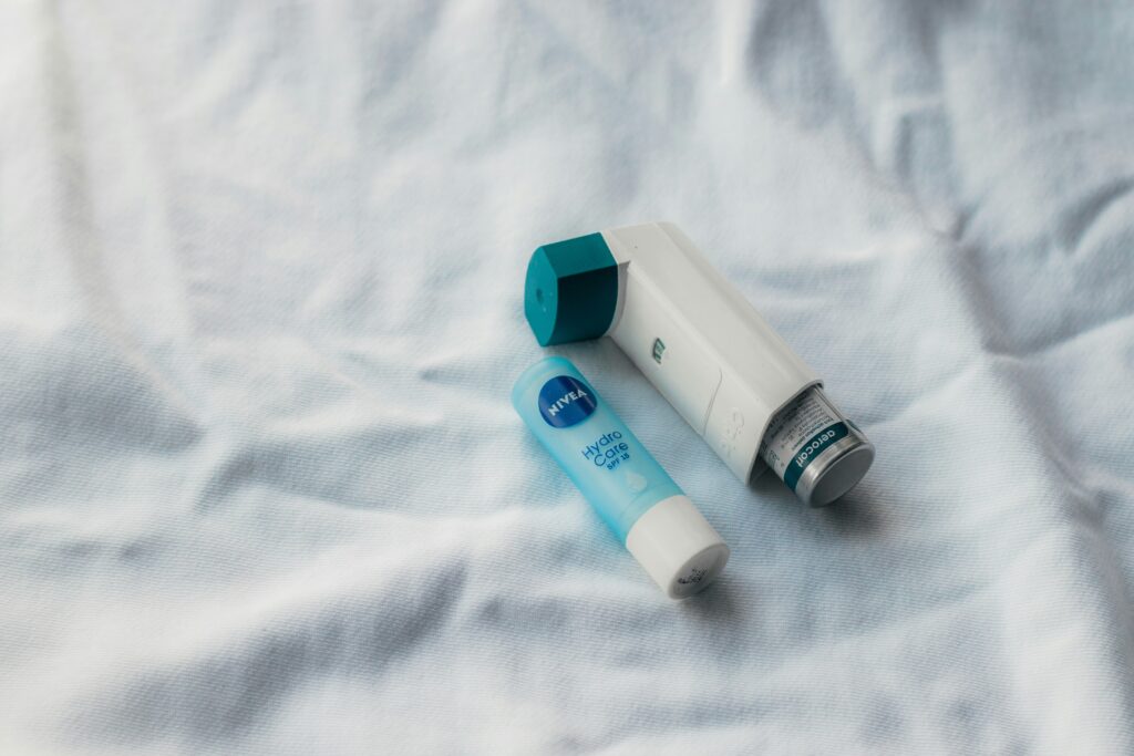 An inhaler and a chapstick on a white bed sheet.