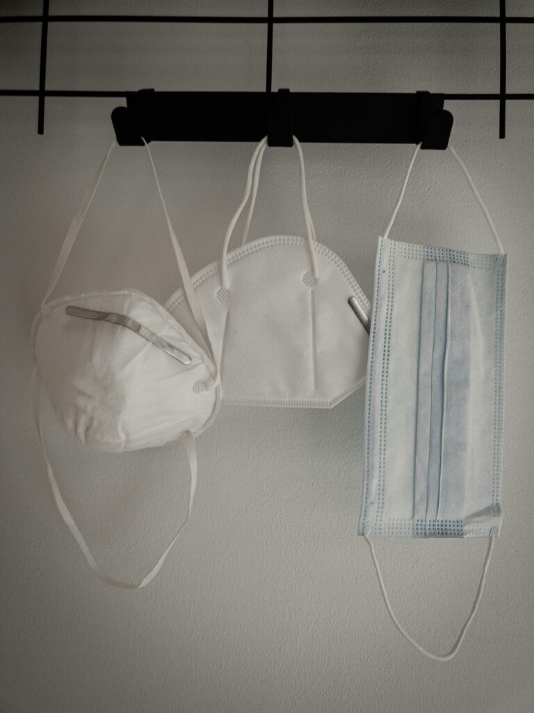 Three types of disposable face masks hanging on black hooks.