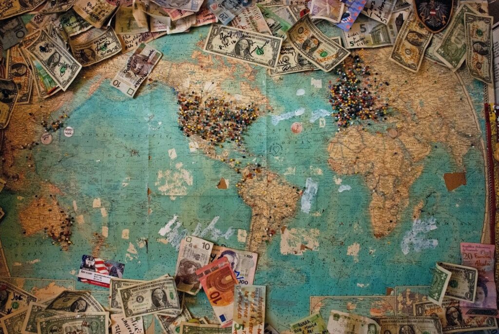 A world map with push pins in major cities surrounded by different currency bills.