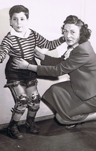 B/W photo of Nina helping young boy stand with leg braces. Circa 1960s