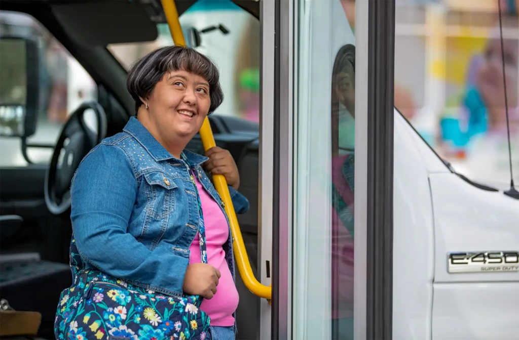 A woman with down syndrome steps off of a bus on a bright day.