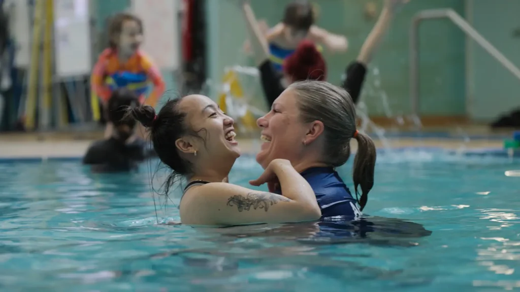 A woman supports another woman while swimming in an indoor pool.