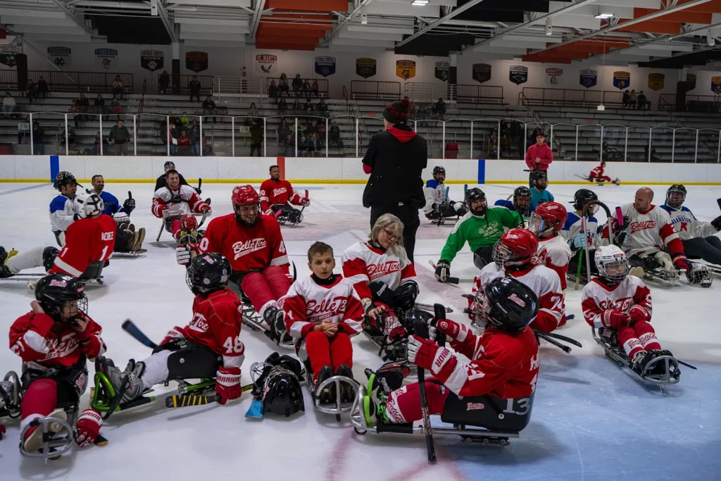 A group of sled hockey players wearing red and white jerseys on the ice.