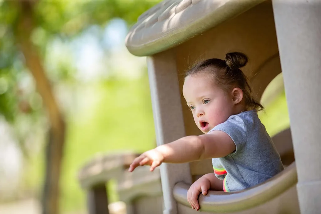 A young girl with Down's Syndrome playing at a playground on a sunny day.