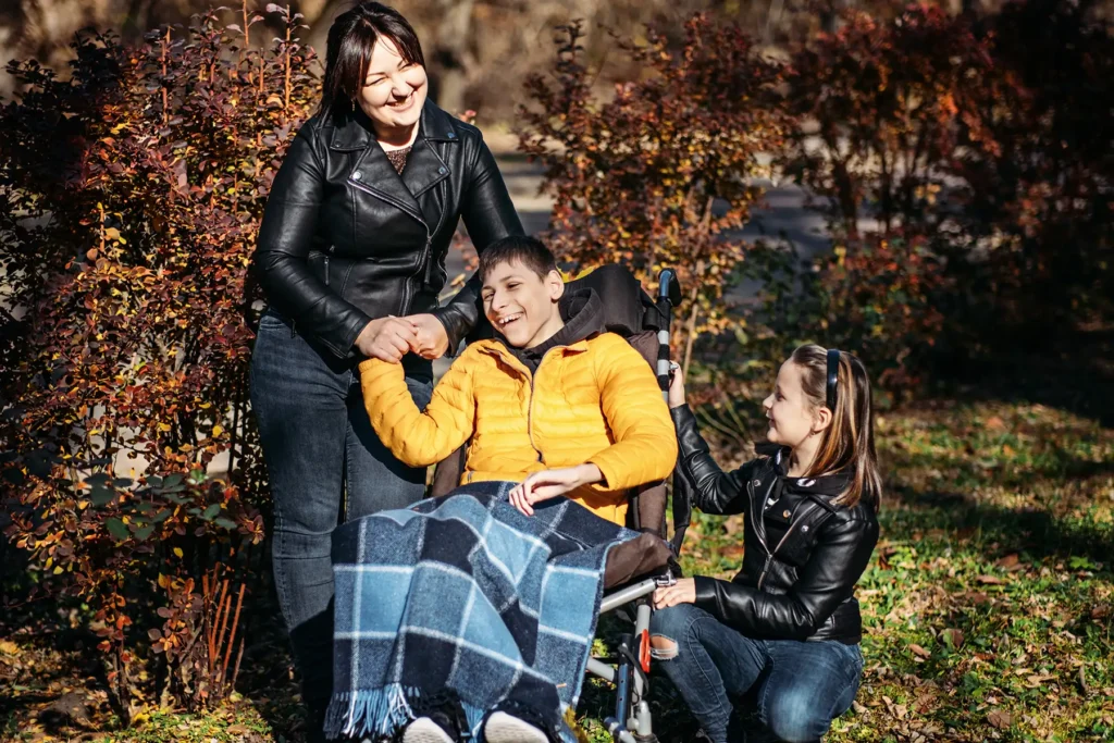 A young man in a wheel chair surrounded by two women who smile with him.