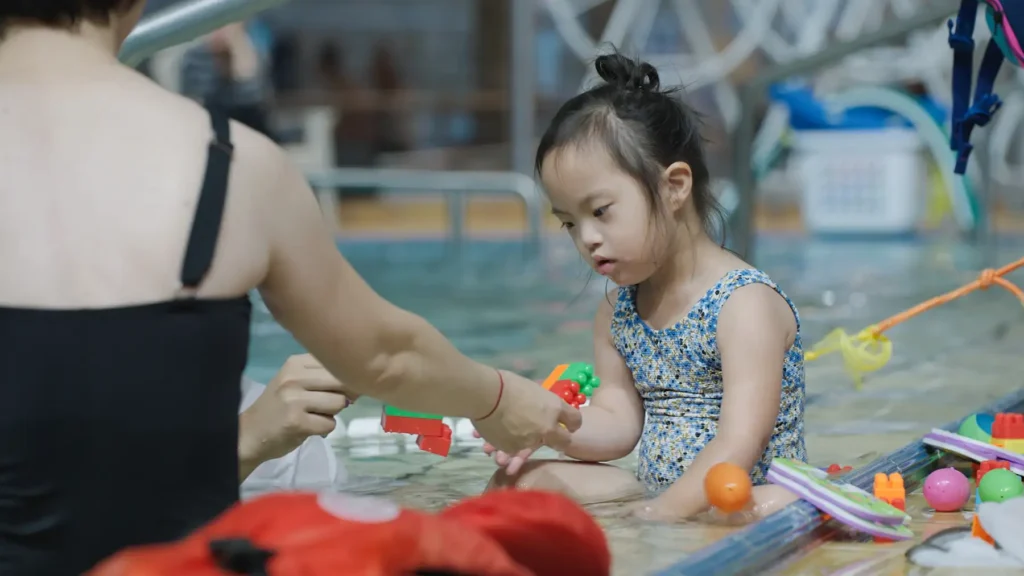 A young girl and her educators play with some water toys in the shallow end of an indoor pool.