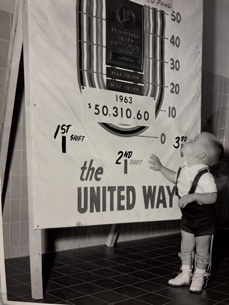 Ken Bluhm as a child, standing next to a United Way fundraising poster.
