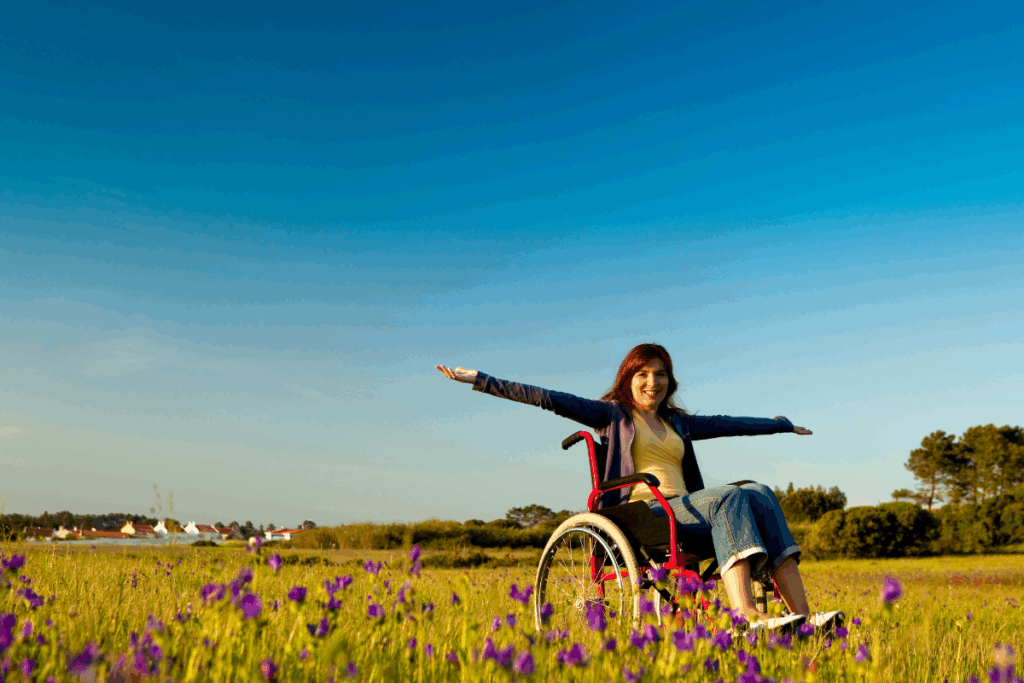 person in a wheelchair who has her arms outstretched while outdoors in a flower field