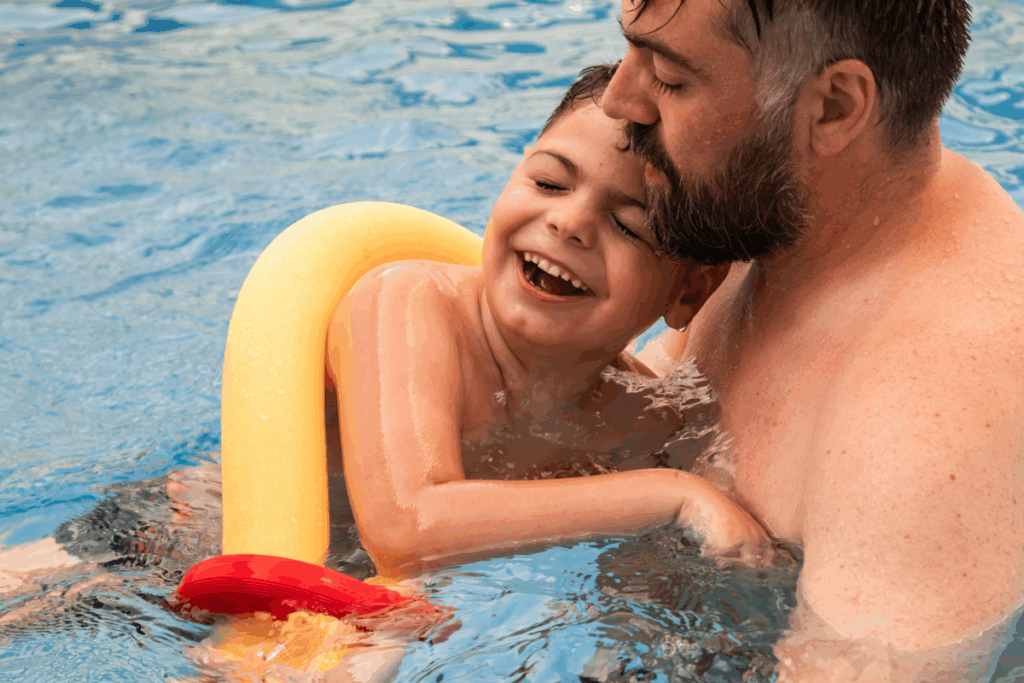 boy with a disability in a swimming pool with his father or caregiver helping. he is smiling