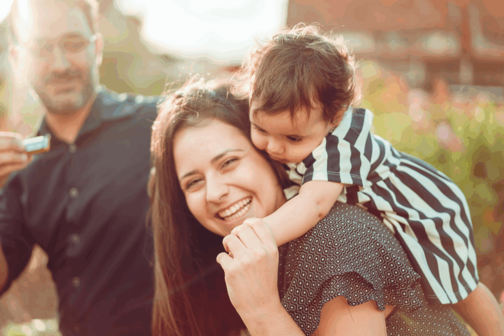 A latino family smiling outdoors. the mother has a baby over her shoulders and they are laughing