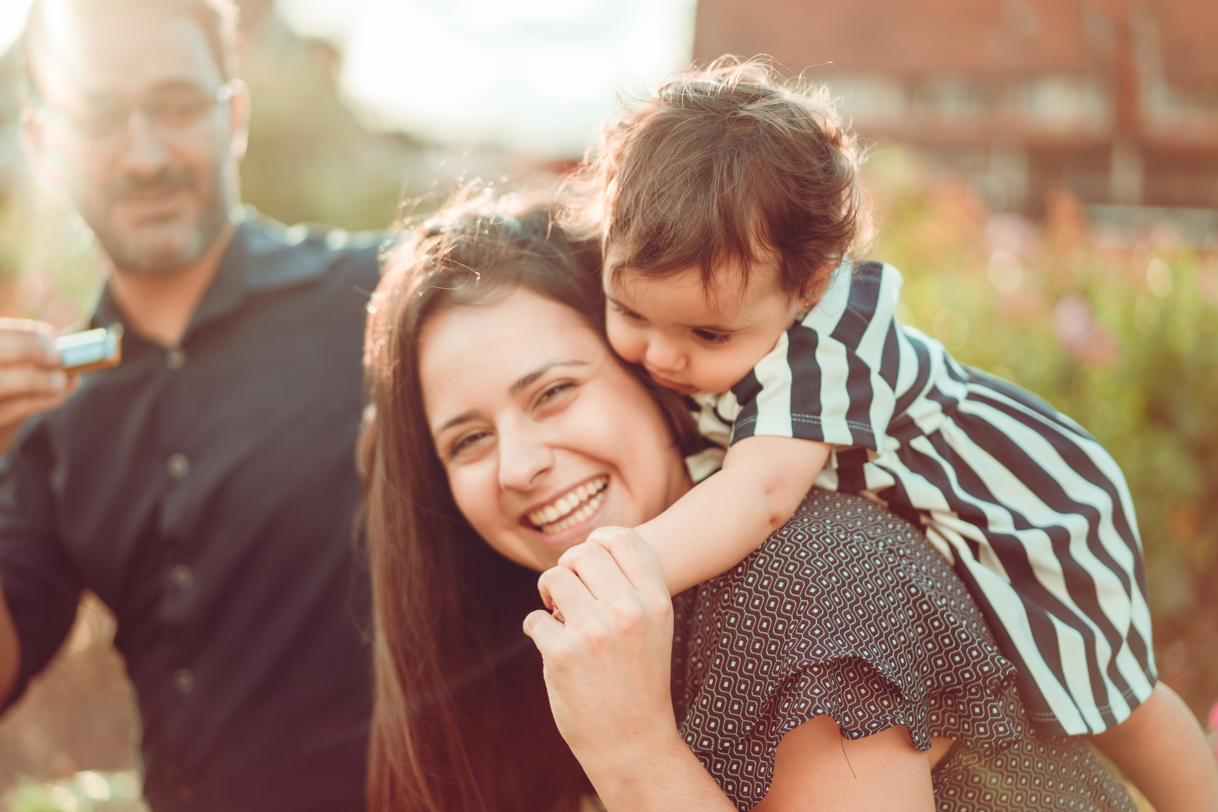 A latino family smiling outdoors. the mother has a baby over her shoulders and they are laughing