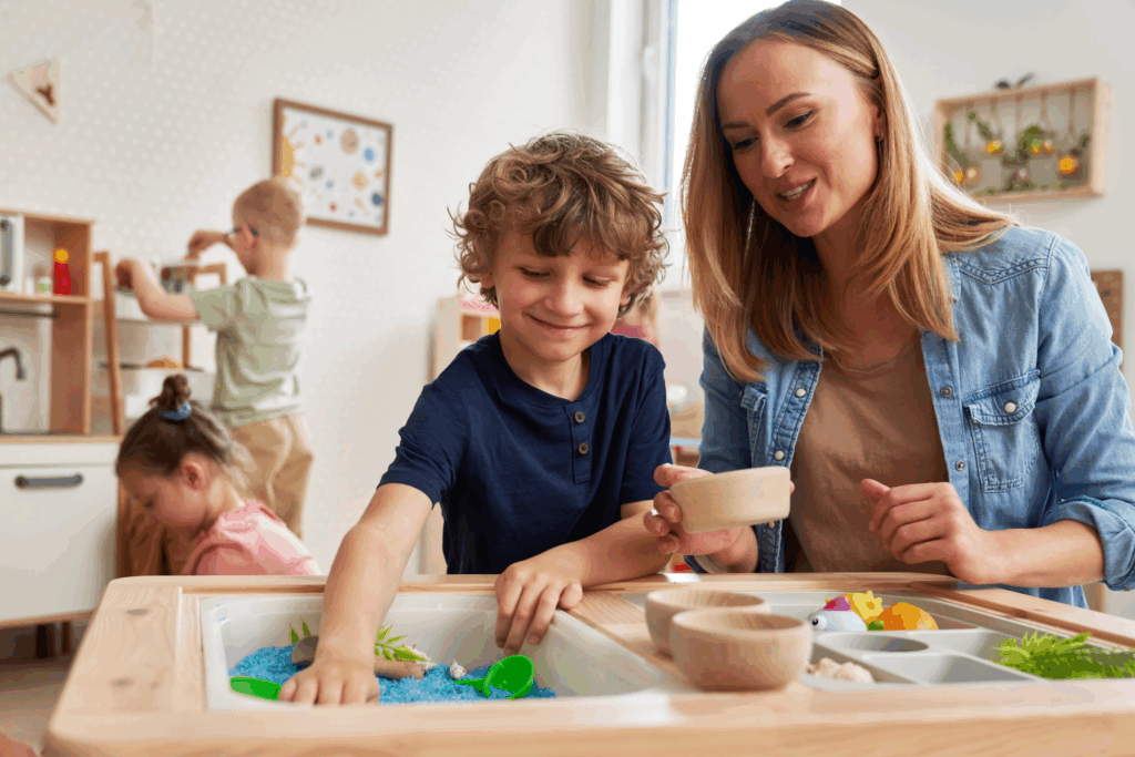 child with a teacher engaging in sensory touch with an indoor sandbox
