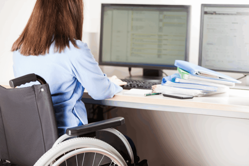 Person in a wheelchair at a desk with a computer and binders of paperwork