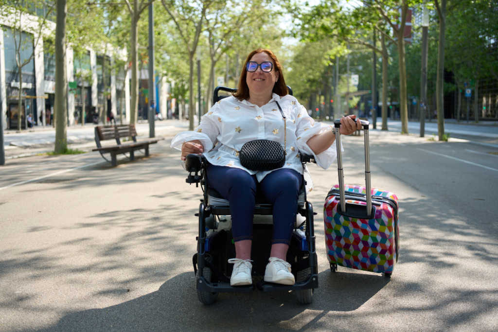 woman in a wheelchair wearing a crossbody bag and pulling a suitcase