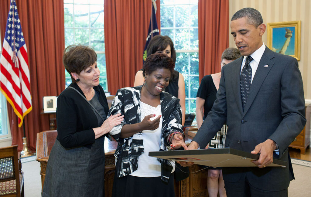 Lois Curtis, the plaintiff in the Olmstead v. L.C. Supreme Court case, ( center) presents Former President Barack Obama with a self-portrait of herself as a child that she painted. Joining them are, from left, Janet Hill and Jessica Long, from the Georgia Department of Labor, and Lee Sanders, of Briggs and Associates. The Oval Office, 20 June 2011. Photo Credit: Official White House Photo by Pete Souza