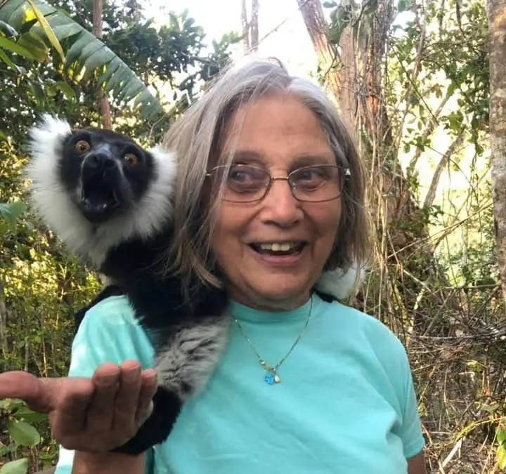 A woman stands in a jungle with an animal on her shoulder