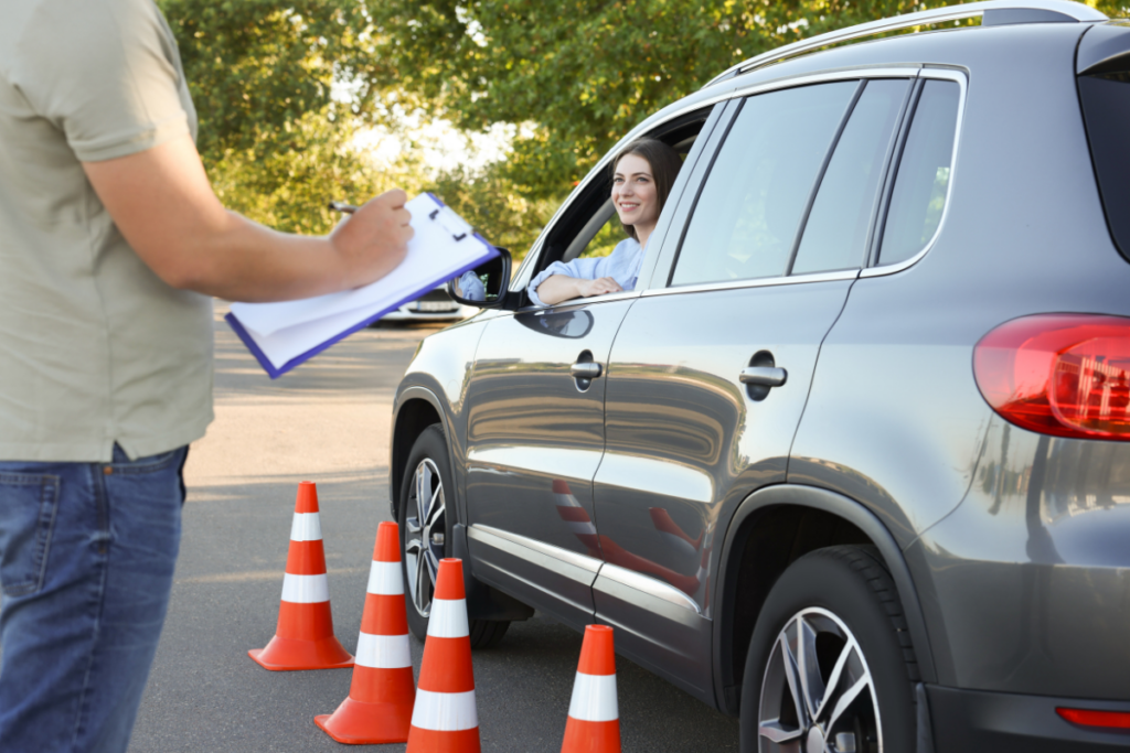 a woman in a car with orange cones along side it taking a driving test